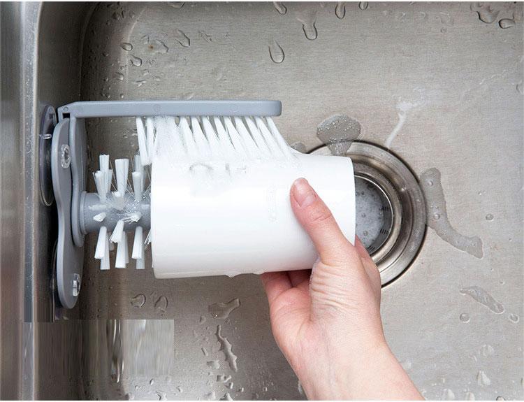 hand washing a glass with a glass cleaning brush attach to the kitchen sink
