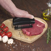 hand pressing meat tenderizer on meat
